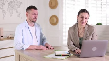 Seyahat acentesi, ofisteki tahta masada oturan adama biletle pasaport veriyor.