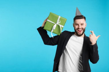 Doğum günün kutlu olsun. Parti şapkası ve hediye kutusu olan yakışıklı bir adam açık mavi arka planda dilek tutarken, mesaj için boşluk yaratıyor.