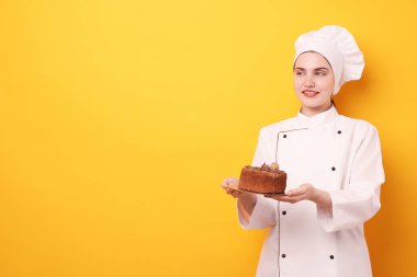 Üniformalı şekerlemeci turuncu arka planda lezzetli çikolatalı pasta tutuyor, mesaj için yer var.