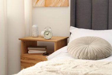 Yatağın yanında alarm saati ve dekorasyonu olan komodinin yanında.