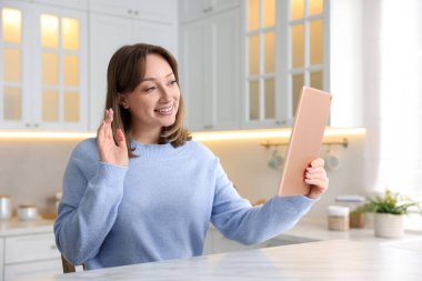 Kadın, mutfaktaki beyaz mermer masada modern tablet vasıtasıyla görüntülü konuşma yapıyor.
