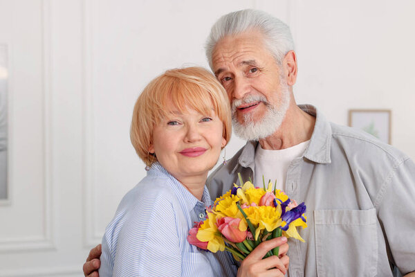 Lovely senior couple with bouquet of flowers at home