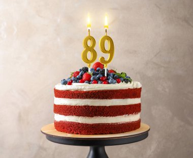 Böğürtlenli lezzetli pasta ve gri duvarın yanında yanan mumlar. 89. yaş günü veya diğer özel günler