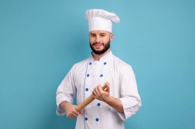 Üniformalı mutlu pastacı açık mavi arka planda merdane tutuyor.