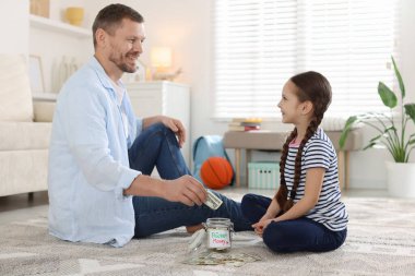 Baba ve kızı evde cep harçlığını kavanoza koyuyorlar.