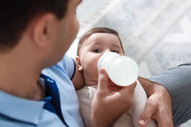 Babası evdeki kanepede bebeğini biberonla besliyor.
