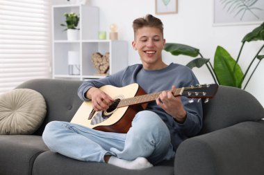 Mutlu adam içeride kanepede gitar çalıyor.
