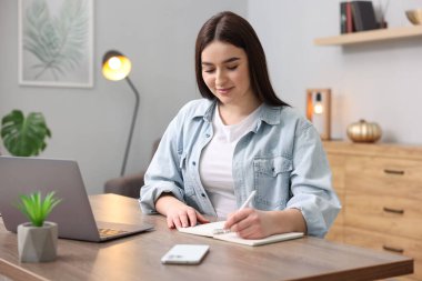 Planlayıcısı olan güzel bir kadın içeride ahşap masada notlar alıyor.
