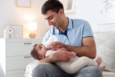 Babası evdeki kanepede bebeğini biberonla besliyor.