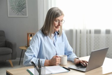 Kapalı mekanda bilgisayarla fincan öğrenen bir kadın. Kendi kendine çalışma.