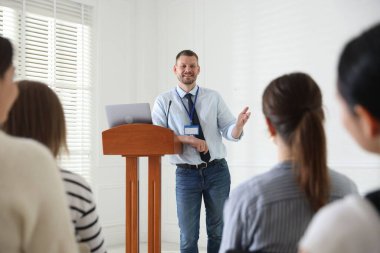 Oturma odasında seyirci önünde konuşma yapan bir adam.