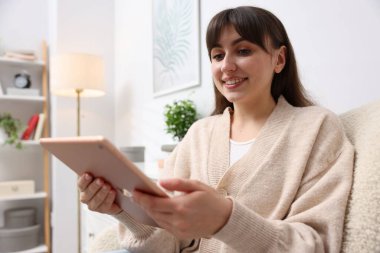 Evdeki koltukta modern tablet kullanan bir kadın.