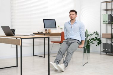 Ofiste sandalyeyle egzersiz yapan yakışıklı adam.