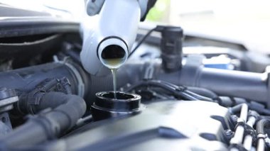İşçi motor yağını teneke kutudan araba motoruna boşaltıyor.