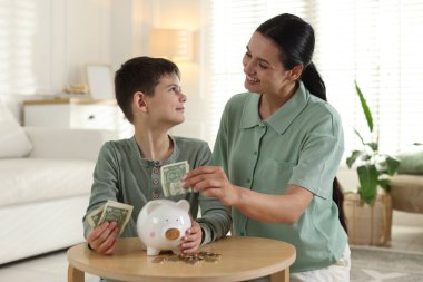 Anne ve oğlu evdeki domuz kumbarasına cep harçlığı koyuyor.