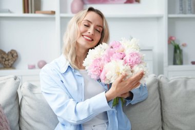 Evdeki kanepede bir buket güzel şakayıklı mutlu kadın.