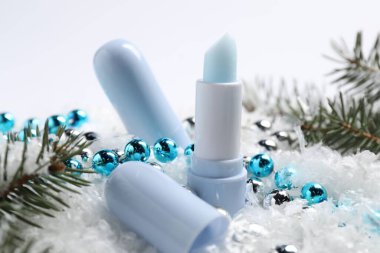 Nemlendirici dudak kremleri, Noel dekorasyonu ve yapay kar üzerindeki köknar ağacı dalları, yakın plan. Kış bakımı