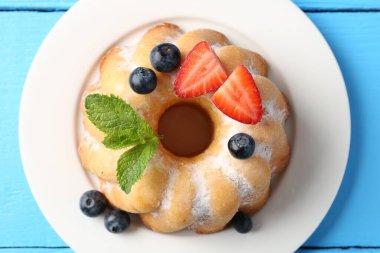 Açık mavi ahşap masada pudra şekeri ve böğürtlenli lezzetli kek.