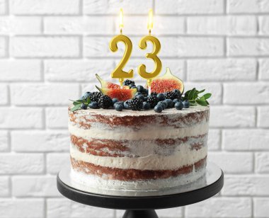 Meyveli lezzetli pasta ve beyaz tuğla duvarın yanında yanan mumlar. 23. yaş günü veya başka özel bir gün.