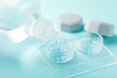 Kontak lens solüsyonunu hafif turkuaz arka planda şişeden kutuya damlatılıyor, yakın plan