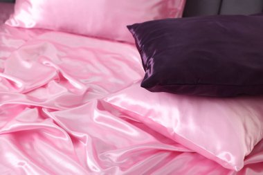 Lüks pembe ipek çarşaflar ve yastıklar yatakta, yakın plan.
