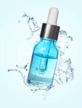 Bir şişe nemlendirici serum ve su açık mavi arka planda havaya sıçrıyor.