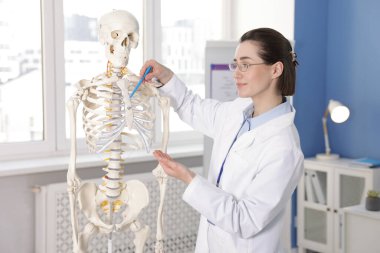 Doktor klinikteki insan iskeleti modelini işaret ediyor.