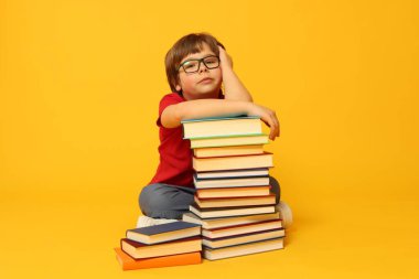 Turuncu arka plan hakkında çok farklı kitapları olan bir çocuk.