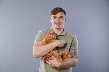 Gri arka planda kızıl kedisi olan sevimli bir adam.