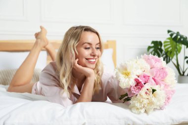 Yatağında şakayık demeti olan mutlu bir kadın.