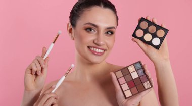 Göz farı paletleri, fırçalar ve pembe arka planda gülümseyen bir kadın olan makyaj sanatçısı.