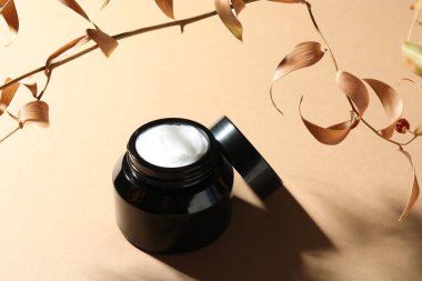 Bej arka planda bir kavanoz vücut kremi ve kuru dallar.