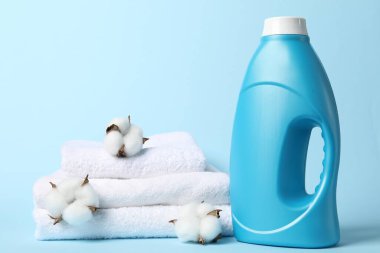 Bir şişe yumuşatıcı, pamuk çiçekleri ve açık mavi arka planda havlular.