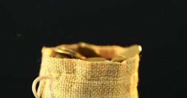 Siyah arkaplanda çuval bezi içine madeni paralar dökülüyor.