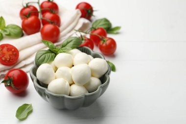Lezzetli mozzarella peyniri topları, domates ve fesleğen beyaz ahşap masada, yakın plan. Metin için boşluk