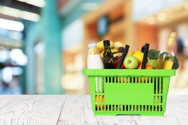 Süpermarketteki ahşap masada içi yiyecek dolu yeşil alışveriş sepeti. Metin için boşluk
