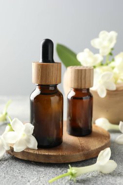 Yağ şişeleri ve yasemin çiçekleri gri masada, yakın plan.