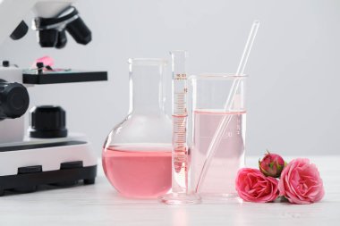 Lüks parfüm yapıyorum. Temel yağlar cam eşyalar, çiçekler ve mikroskop beyaz ahşap masa üzerinde, yakın çekim