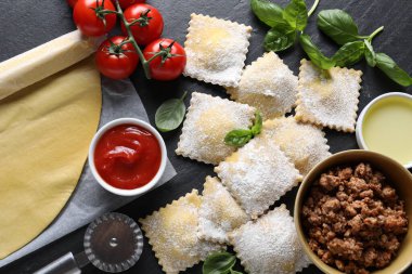 Pişmemiş ravioli, bolonez, sos, domates ve fesleğen siyah masada, düz yatıyordu.