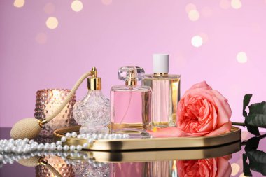 Ayna yüzeyinde birçok farklı parfüm şişesi, çiçek ve aksesuar var. Pembe arka plan, bulanık ışıklar, yakın plan.