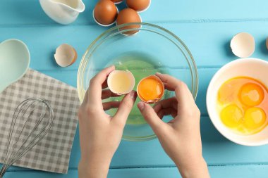 Açık mavi ahşap masada yumurta sarısını beyazdan ayıran kadın.