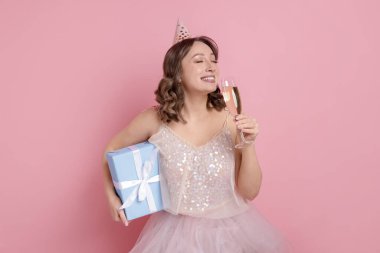 Doğum günü kutlaması. Bir bardak köpüklü şarap ve pembe arka planda bir hediye.