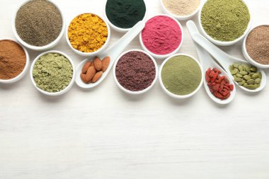 Beyaz ahşap masa üzerinde farklı süper yiyecek tozları, düz yatış. Metin için boşluk