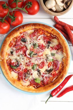 İnce tütsülenmiş sosis ve beyaz ahşap masa üzerindeki malzemelerle nefis bir pizza.