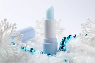 Nemlendirici dudak kremi ve yapay kar üzerine Noel süsü, yakın plan. Kış bakımı