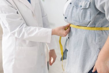 Kilo kaybı. Klinikte kilolu kadının belini bantla ölçen beslenme uzmanı.