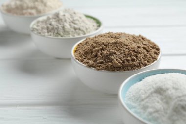 Beyaz ahşap masadaki kaselerdeki farklı un türleri, yakın plan.