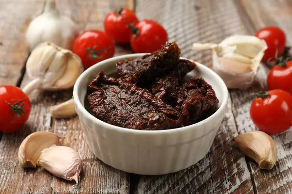 Lezzetli güneşte kurutulmuş domatesler, taze sebzeler ve ahşap masada sarımsak, yakın plan.