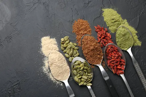 Siyah masadaki kaşıklarda farklı süper yiyecekler, düz yatış. Metin için boşluk