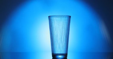 Bir kadın masadaki bardağa su dolduruyor. Arka plan mavi, yakın plan. Arka ışıklandırma